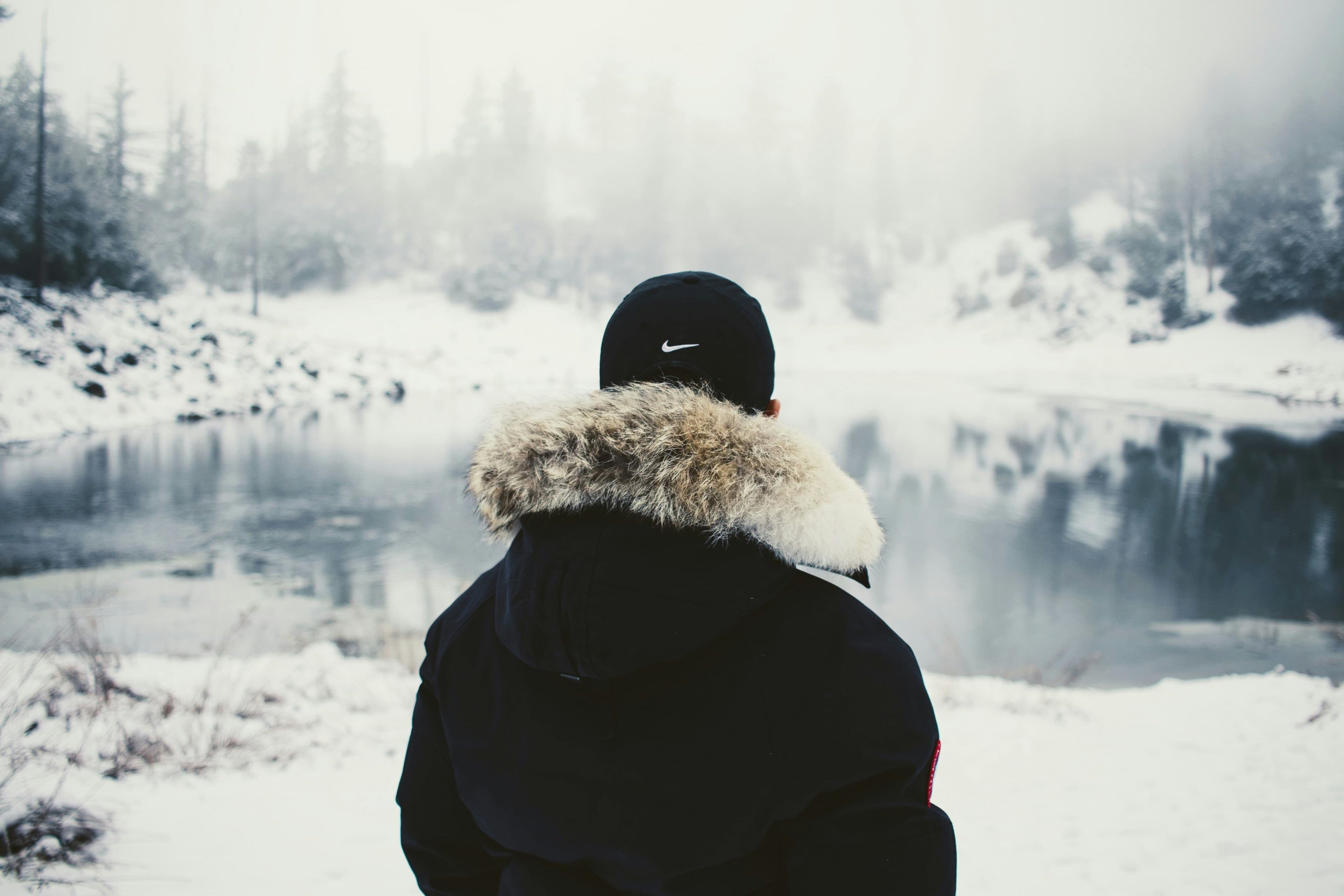 Mann in schwarzer Jacke steht vor einem See